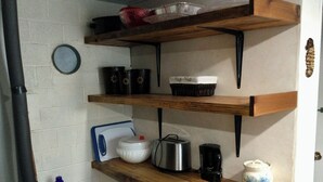 A kitchen with wooden shelves holding various kitchen items, a coffee maker, and a trash bin. - Sea Shell Inn. A cozy hideaway (Duncan)