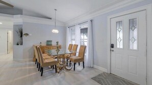 Un coin repas avec une table et des chaises en verre, un lustre et une porte blanche ornée de vitraux.