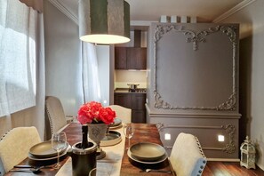 Zona pranzo con tavolo in legno, sedie, un vaso di fiori rossi e un pannello decorativo a parete.