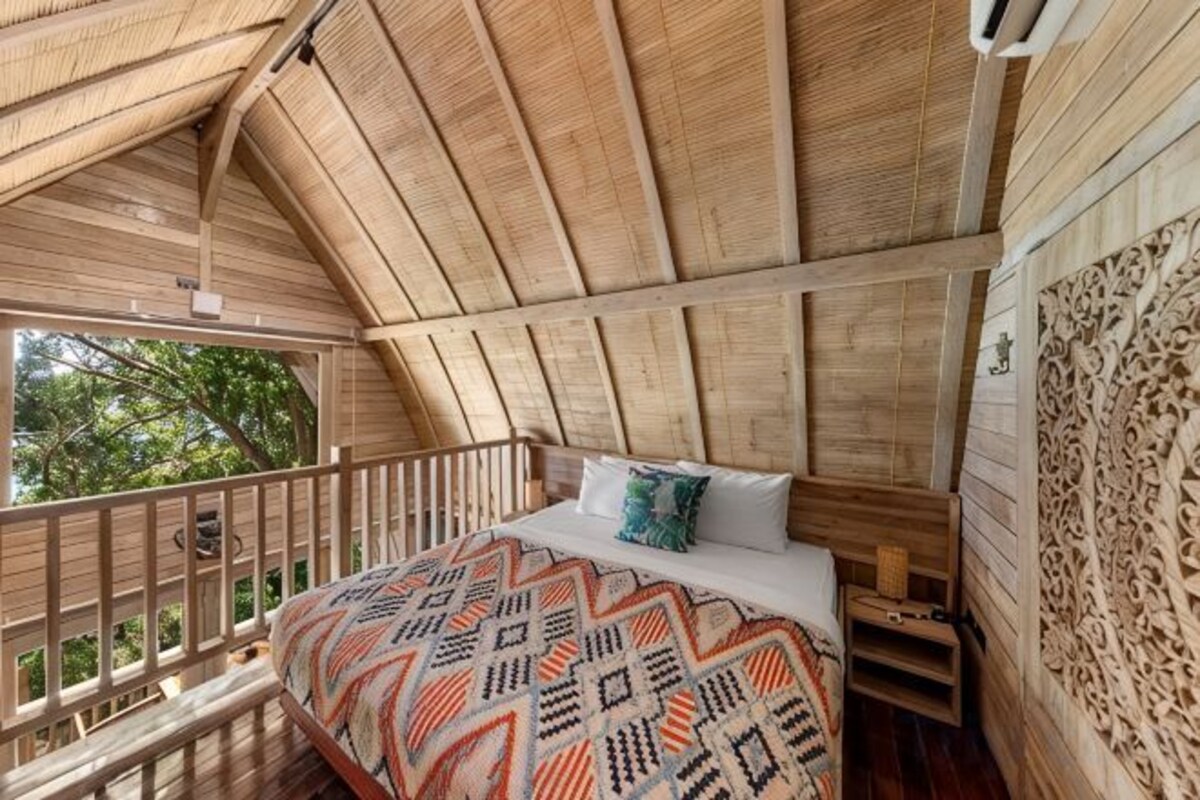 A bedroom with a bed, pillows, and a wooden ceiling.
