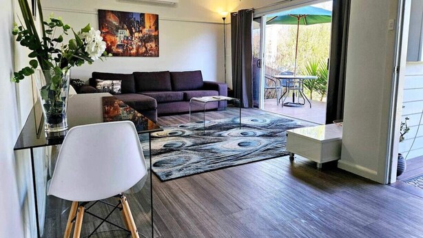 A modern living room with a sofa, a coffee table, and a chair. There is a painting on the wall and a window with curtains. - Quantrill Avenure Retreat (Benalla)