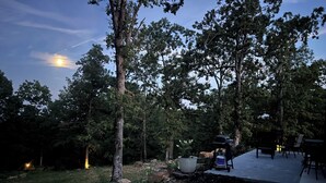 An outdoor patio area with a barbecue grill, seating, and a view of the surrounding trees.