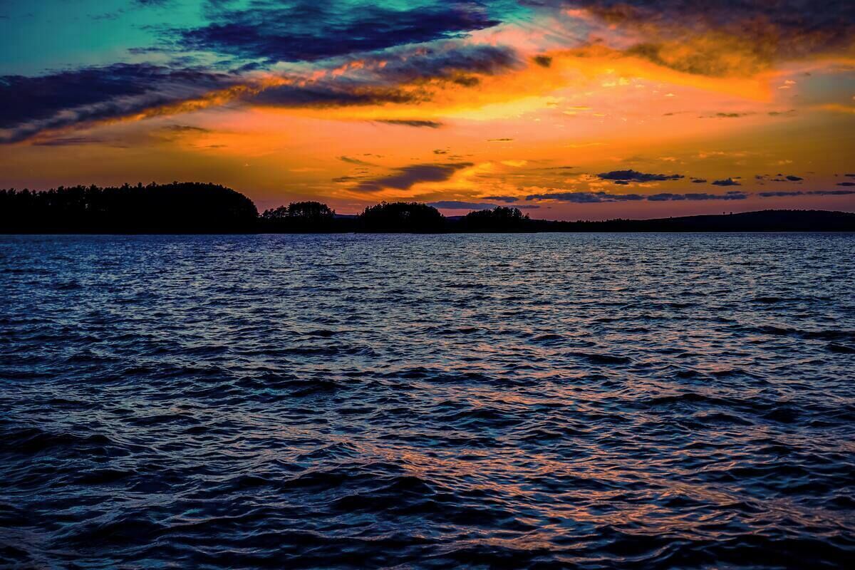 Un coucher de soleil sur une étendue d’eau, avec la silhouette d’une masse terrestre visible au loin.