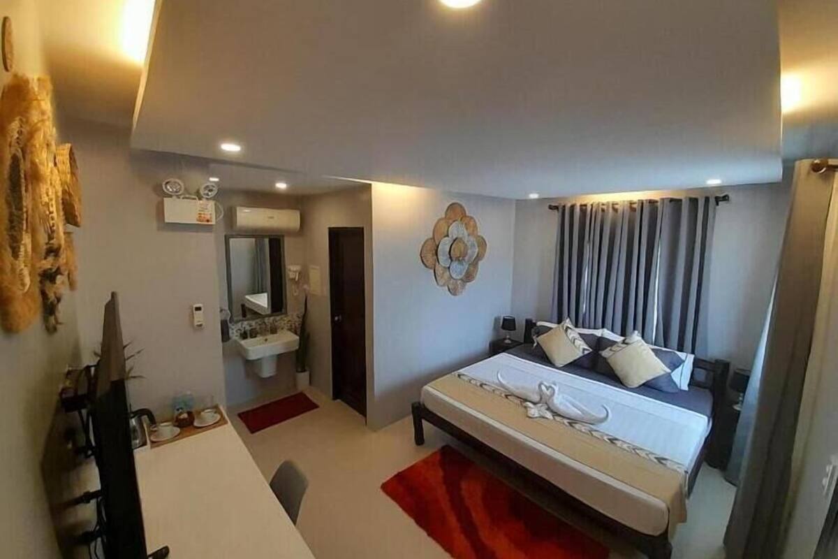 A modern hotel room with a bed, bedside table, and a bathroom with a sink and mirror.