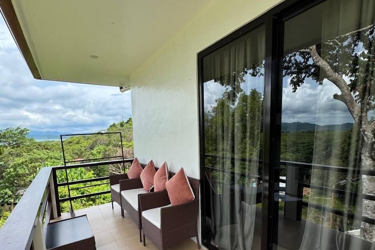 A balcony with a sofa and chairs, a table, and a view of greenery.