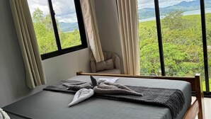 Une chambre à coucher avec un lit, des rideaux et une vue sur la verdure et les montagnes.