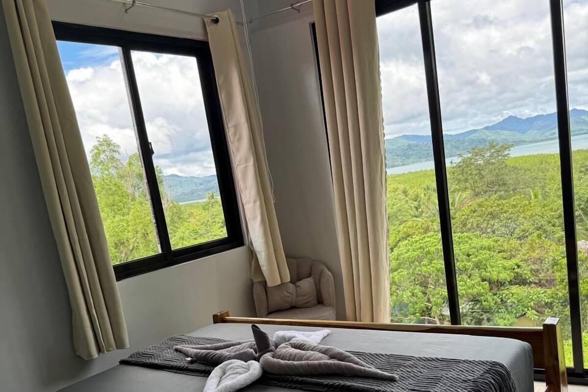 A bedroom with a bed, curtains, and a view of greenery and mountains.