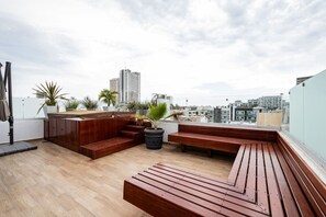 Une terrasse sur le toit, avec des bancs en bois, des plantes en pot et une vue sur le paysage urbain.