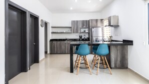 Una cocina moderna con armarios oscuros, encimera negra y dos taburetes azules.