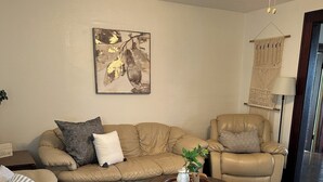 A living room with a beige sofa, a chair, a coffee table, a wall-mounted macrame, and a ceiling fan.