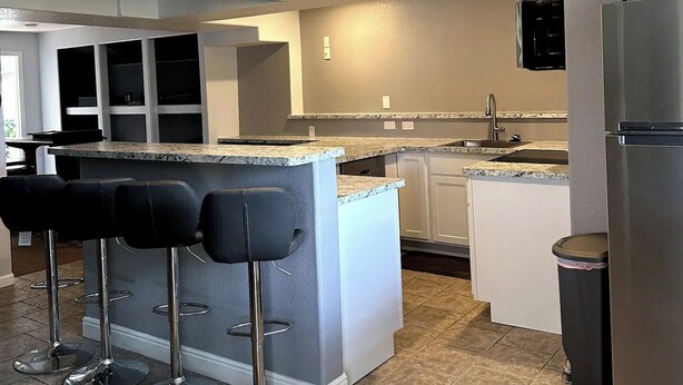 Una cocina moderna con una isla central, taburetes de bar, un refrigerador y un lavamanos.