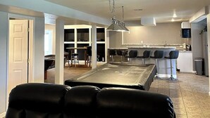 Una sala moderna con mesa de billar, sillas de cuero negro y una zona de bar con taburetes.