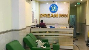 A hotel reception area with a reception desk, a man standing behind it, and green seating areas. - Dream Hotel (Nha Trang)