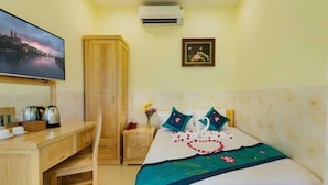 A hotel room with a bed, a TV, a wardrobe, a desk with a kettle, and a small nightstand with a vase of flowers. - Dream Hotel (Nha Trang)