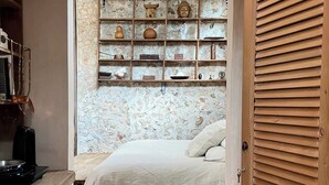 Une chambre à coucher avec un lit, une porte en bois et une étagère fixée au mur, sur laquelle sont disposés divers objets.
