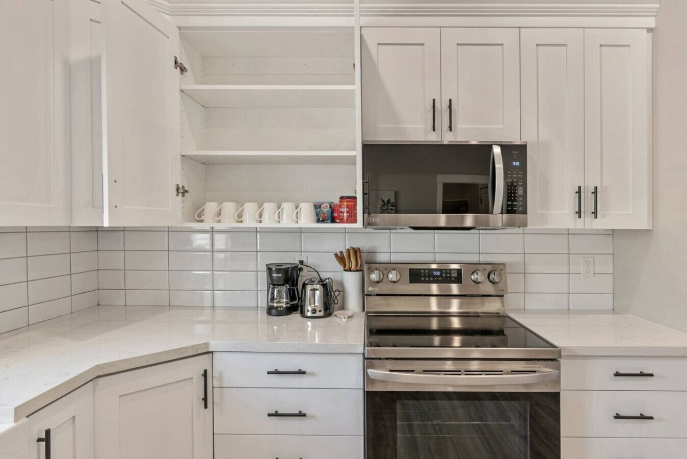 A modern kitchen with white cabinetry, a stainless steel oven, a microwave, and a coffee maker.
