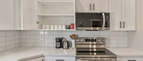 A modern kitchen with white cabinetry, a stainless steel oven, a microwave, and a coffee maker.