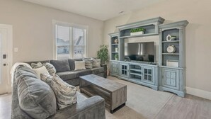 A living room with a gray sectional sofa, a coffee table, a TV cabinet with shelves, and a ceiling fan. - New! Main Street Retreat | BBQ | Pac-Man (Lehi)