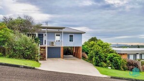 A two-story house with a garage, surrounded by lush greenery. - Caves Cottage - gorgeous 180 degree ocean views (Caves Beach)
