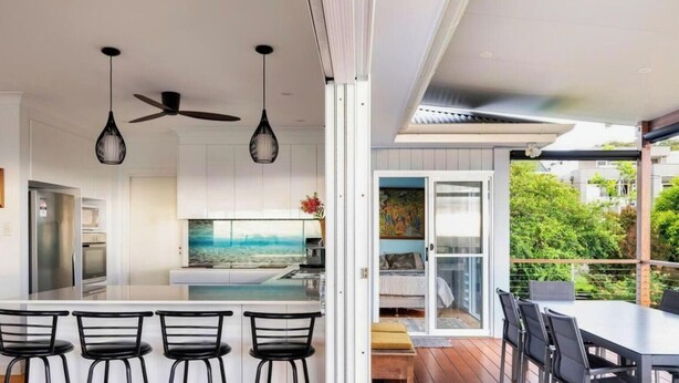 A modern kitchen with a central island, bar stools, pendant lighting, and a ceiling fan. - Caves Cottage - gorgeous 180 degree ocean views (Caves Beach)