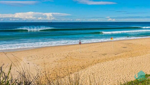 A beach with clear skies, waves, and a no swimming sign.