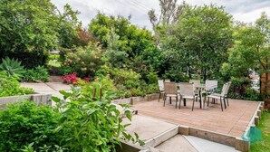 A patio with a table and chairs, surrounded by lush greenery and a variety of plants.