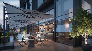 An outdoor seating area with tables and chairs, large umbrellas, and a bar area with a glass enclosure.