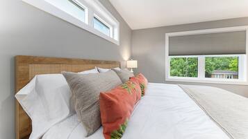Une chambre à coucher avec un grand lit, une tête de lit, deux fenêtres et une vue sur la verdure.