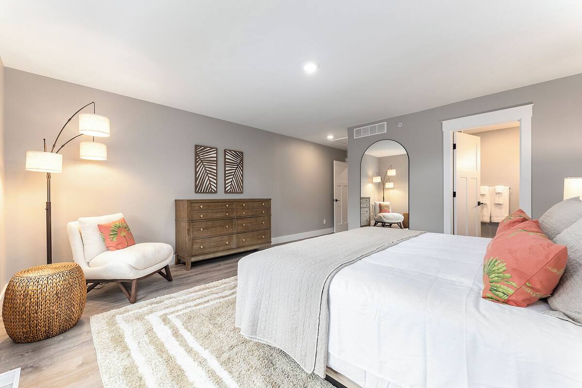 Un dormitorio moderno con una cama grande, un aparador, una silla y una lámpara de pie.