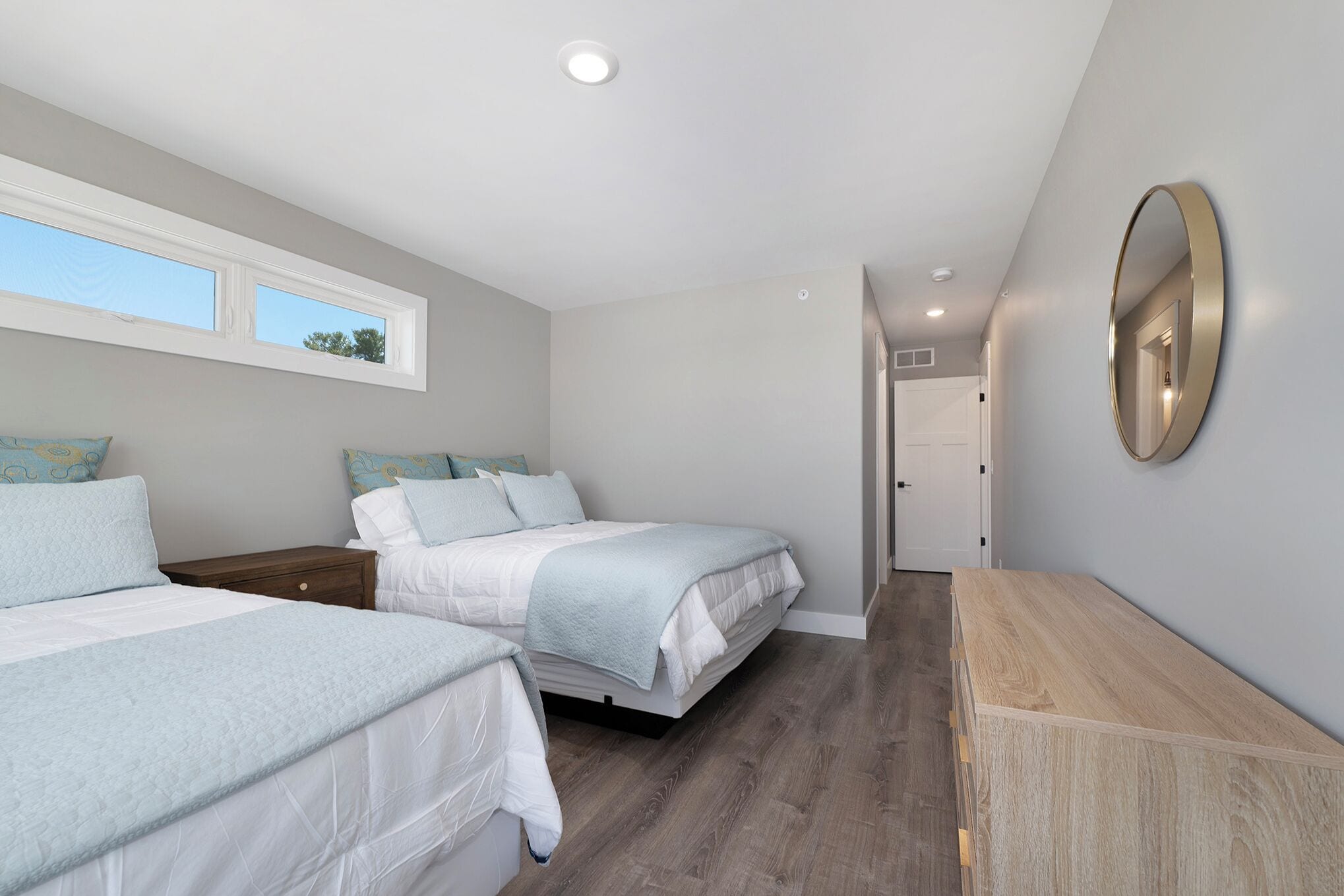 Een slaapkamer met twee bedden, een houten dressoir, een spiegel en een raam.