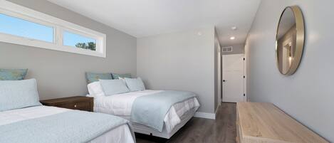 A bedroom with two beds, a wooden dresser, a mirror, and a window.