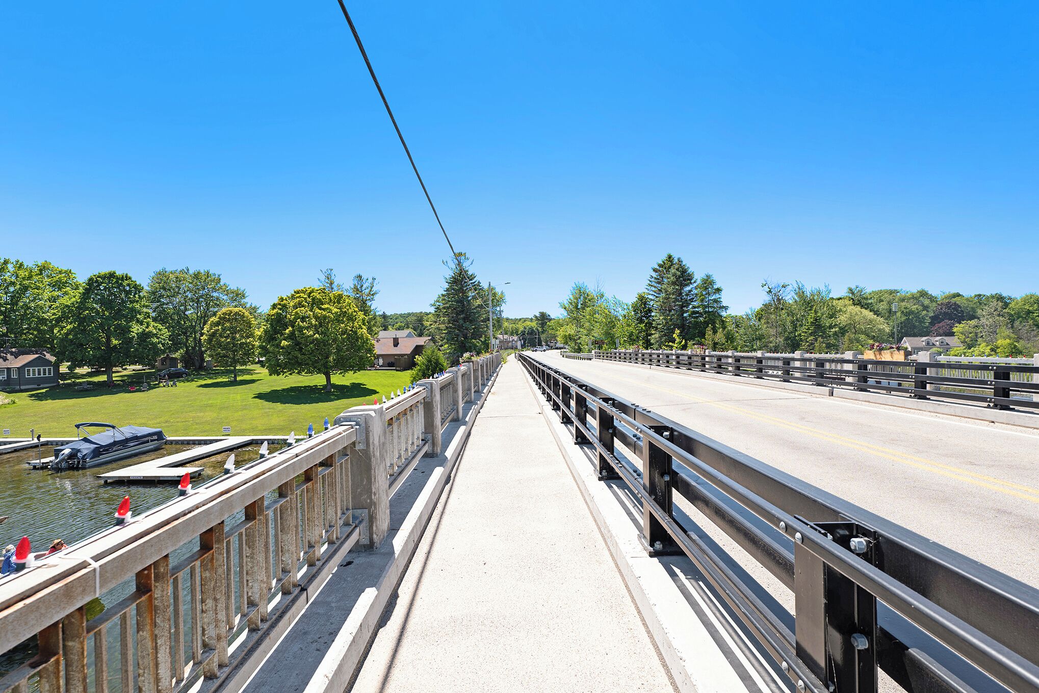 A bridge with a clear view of the river below, a pedestrian walkway, and a distant view of houses and trees.