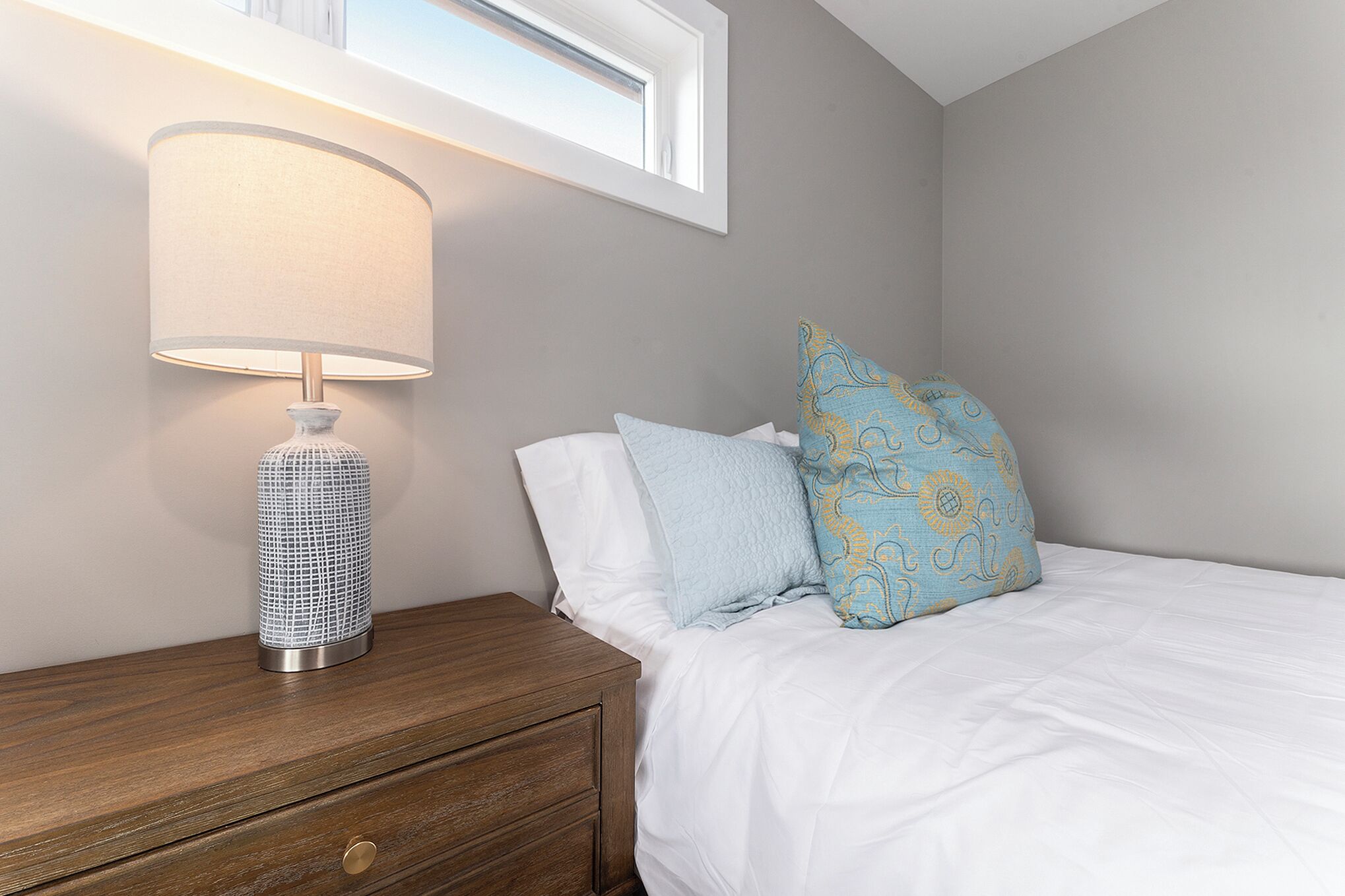 A bedroom with a bed, a nightstand, a lamp, and a window.