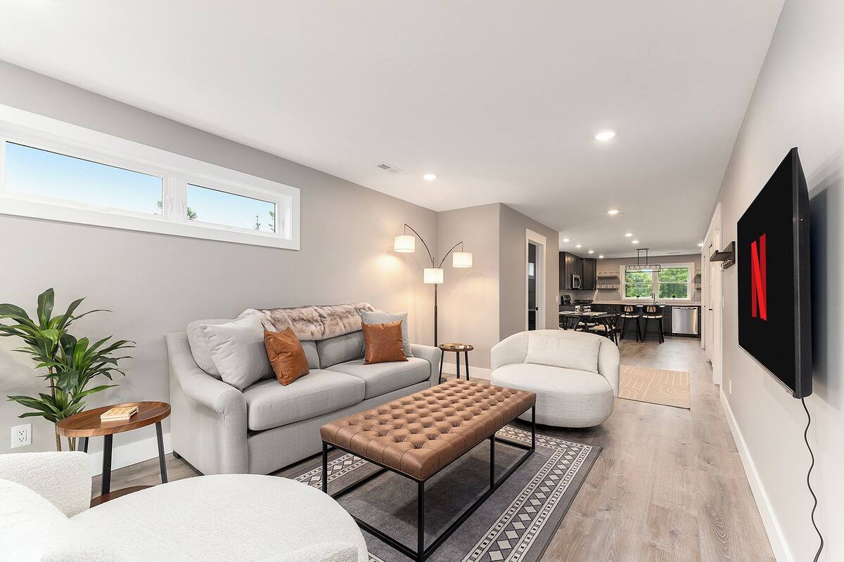 Una sala de estar moderna con un sofá, un sillón y un reposapiés, un comedor y una cocina al fondo.