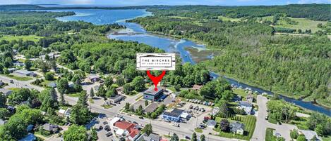 Vista aérea de un pequeño pueblo con un edificio destacado identificado como "The Birches of Lake Leelanau", rodeado de abundante vegetación y un lago.