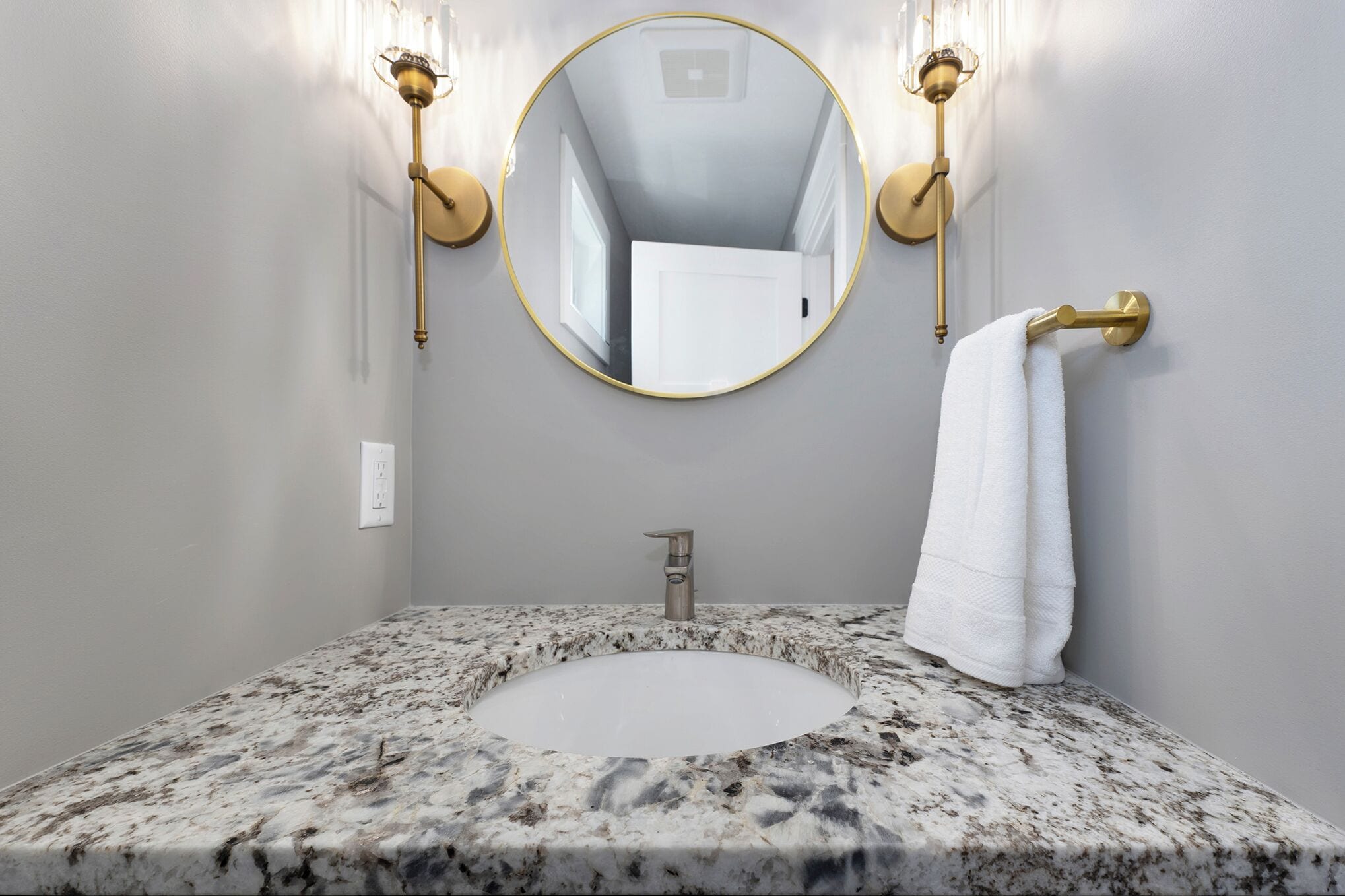 A bathroom with a granite sink, gold-framed mirror, and wall-mounted lights.