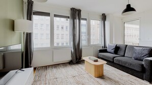 A modern living room with a grey sofa, a wooden coffee table, and a large window with curtains.