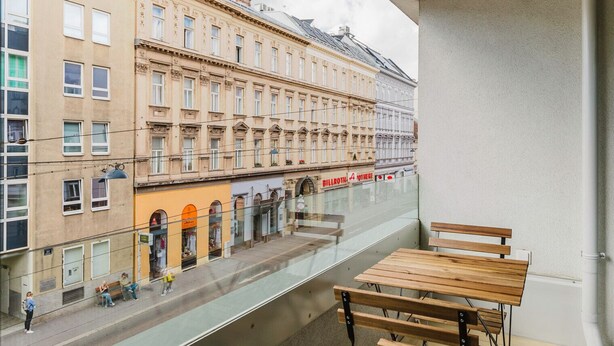 A balcony with a view of a street, a wooden table, and a bench.