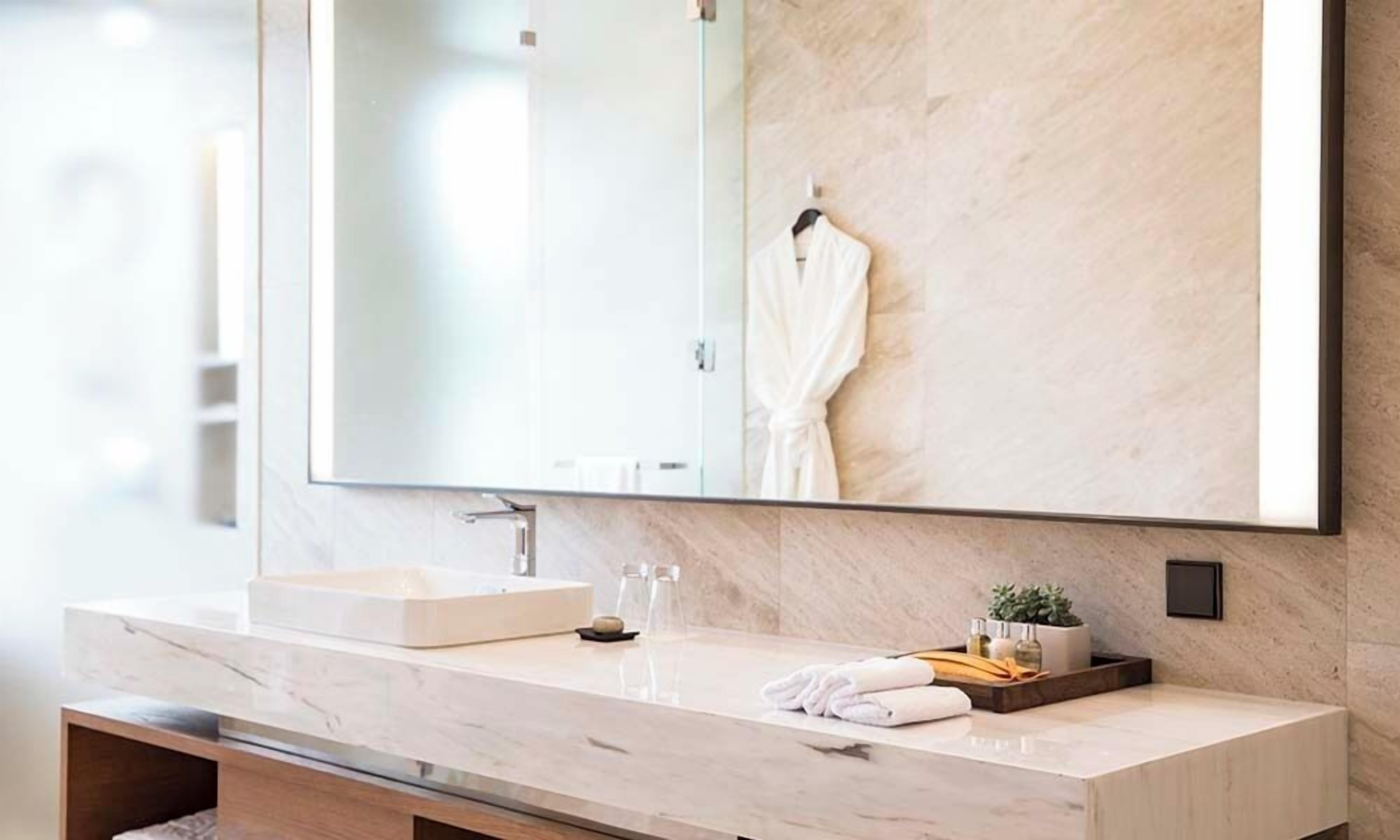 A modern bathroom with a large mirror, a marble countertop, a sink, and a towel rack.