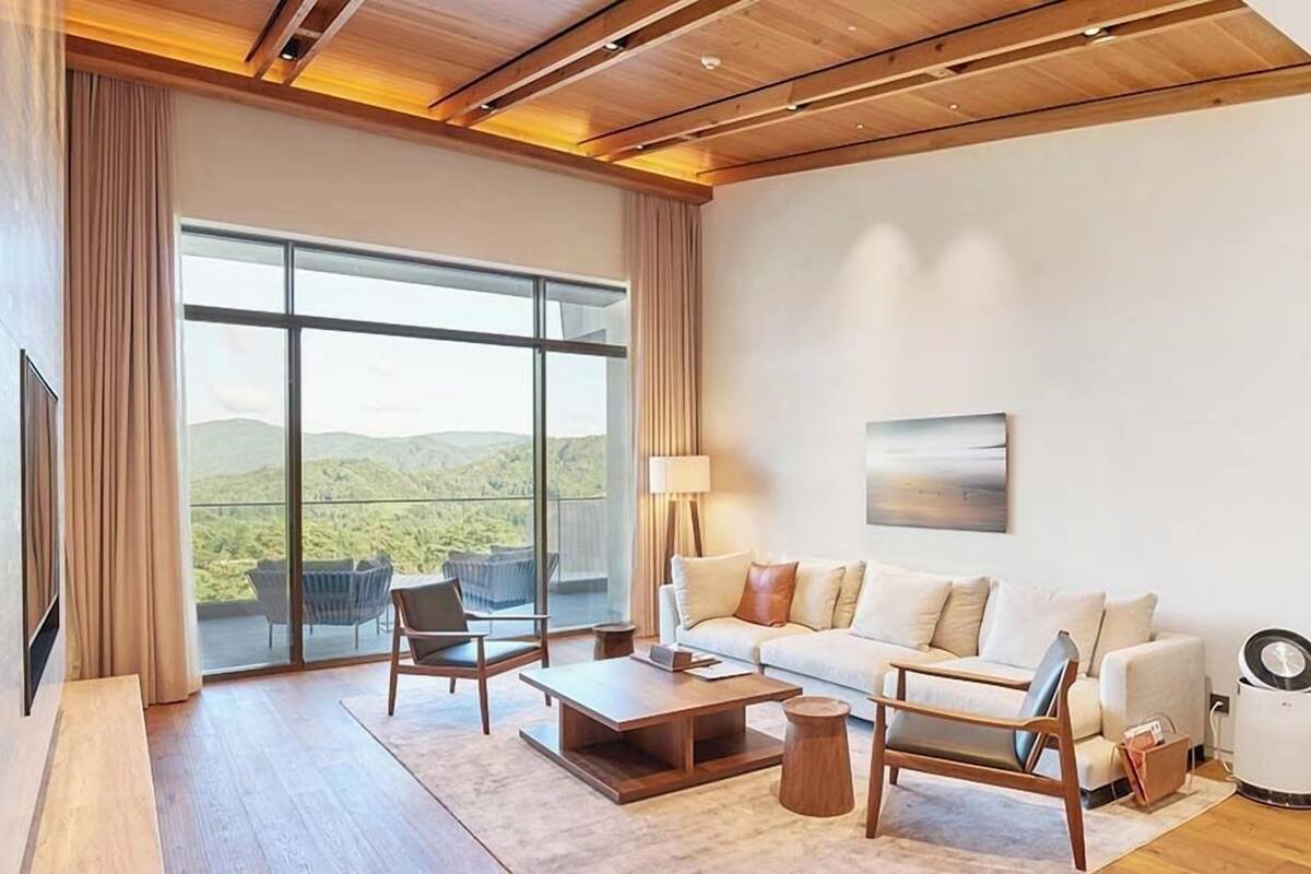 A spacious living room with a large window, a sofa, a coffee table, and a lamp.