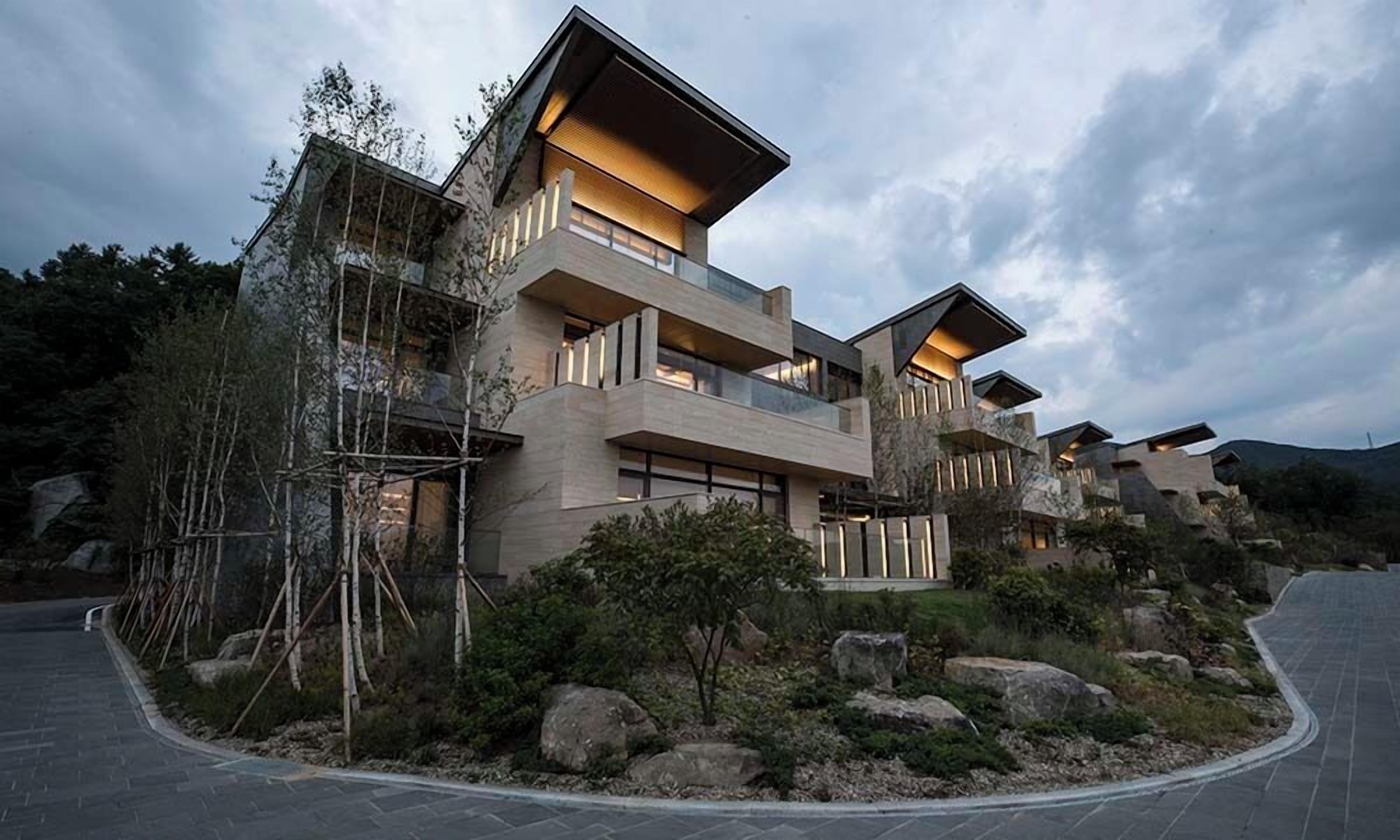 Un edificio moderno de varios pisos con fachada de piedra, amplias ventanas e iluminación exterior.