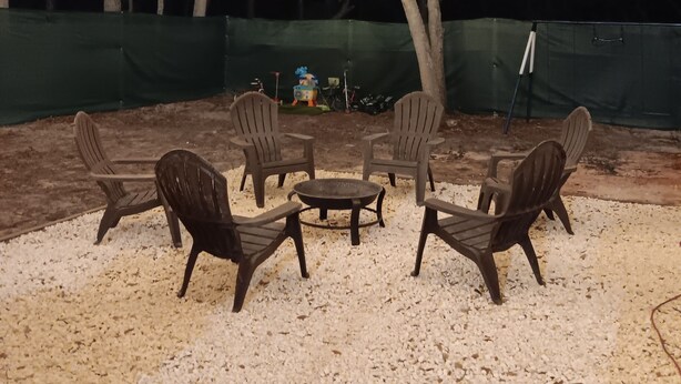 Ein Sitzbereich im Freien mit Stühlen und Tisch, umgeben von Bäumen und Lichterketten.