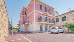 A multi-story pink building with balconies, a parking area, and a white car parked in front. - Merlo C - Center & Private Parking, Ceriale, Italy (Ceriale)