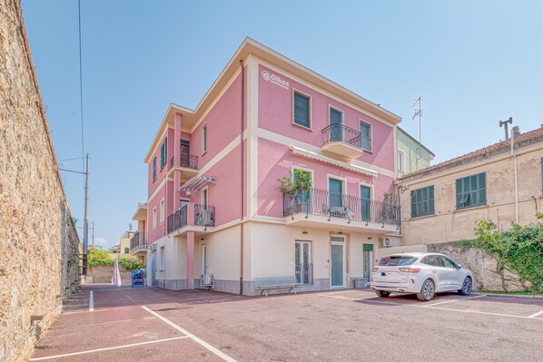 A multi-story pink building with balconies, a parking area, and a white car parked in front.