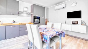 Une cuisine moderne avec des meubles gris, un four encastré et un four à micro-ondes. On y trouve une table à manger avec des chaises et une nappe colorée.