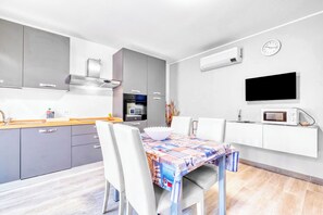 A modern kitchen with grey cabinets, a built-in oven, and a microwave. There is a dining table with chairs and a colorful tablecloth. - Merlo C - Center & Private Parking, Ceriale, Italy (Ceriale)