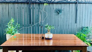 Une table en bois, accompagnée d’un banc, placée contre une clôture en bois surmontée d’un motif de feuilles.