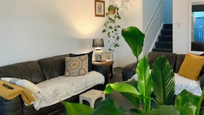 Un salon avec un canapé en cuir foncé, un plaid blanc et moelleux, une petite table avec une lampe et une plante suspendue.