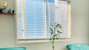 Une chambre avec deux lits, une fenêtre avec des stores, un globe terrestre et une petite plante.