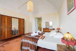 Ein Schlafzimmer mit einem Bett, einem Kleiderschrank, einem Spiegel, einer Lampe und einer Tür zu einem anderen Raum.